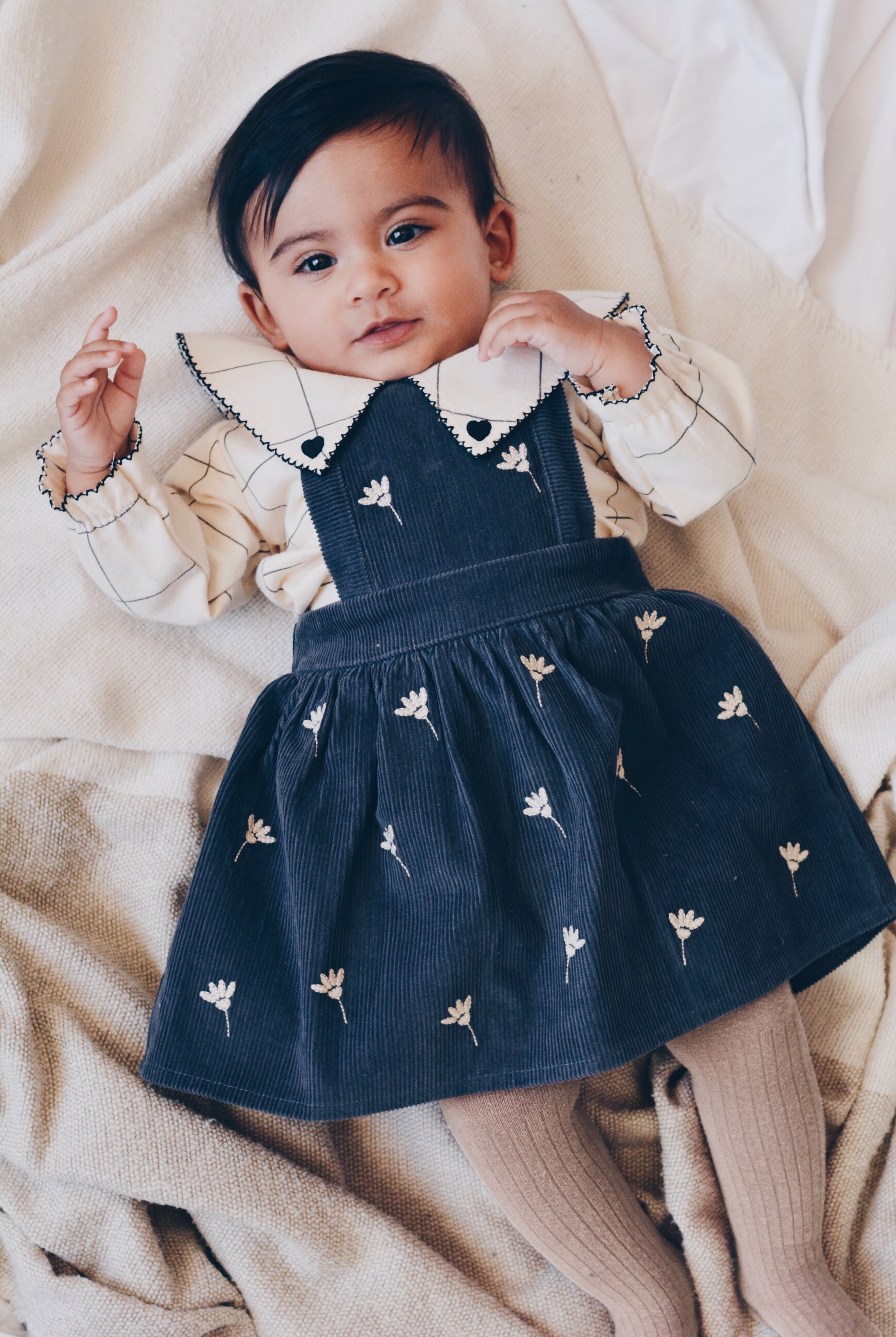 Shop the DALILA Blouse by Eli & Nev — a baby and toddler blouse in 100% OEKO-TEX certified cotton. Designed with a faded black check on beige, black trim with heart embroidery, elastic cuffed sleeves, and coconut button closure. Ethically made in Turkey, perfect for stylish and comfortable everyday wear.