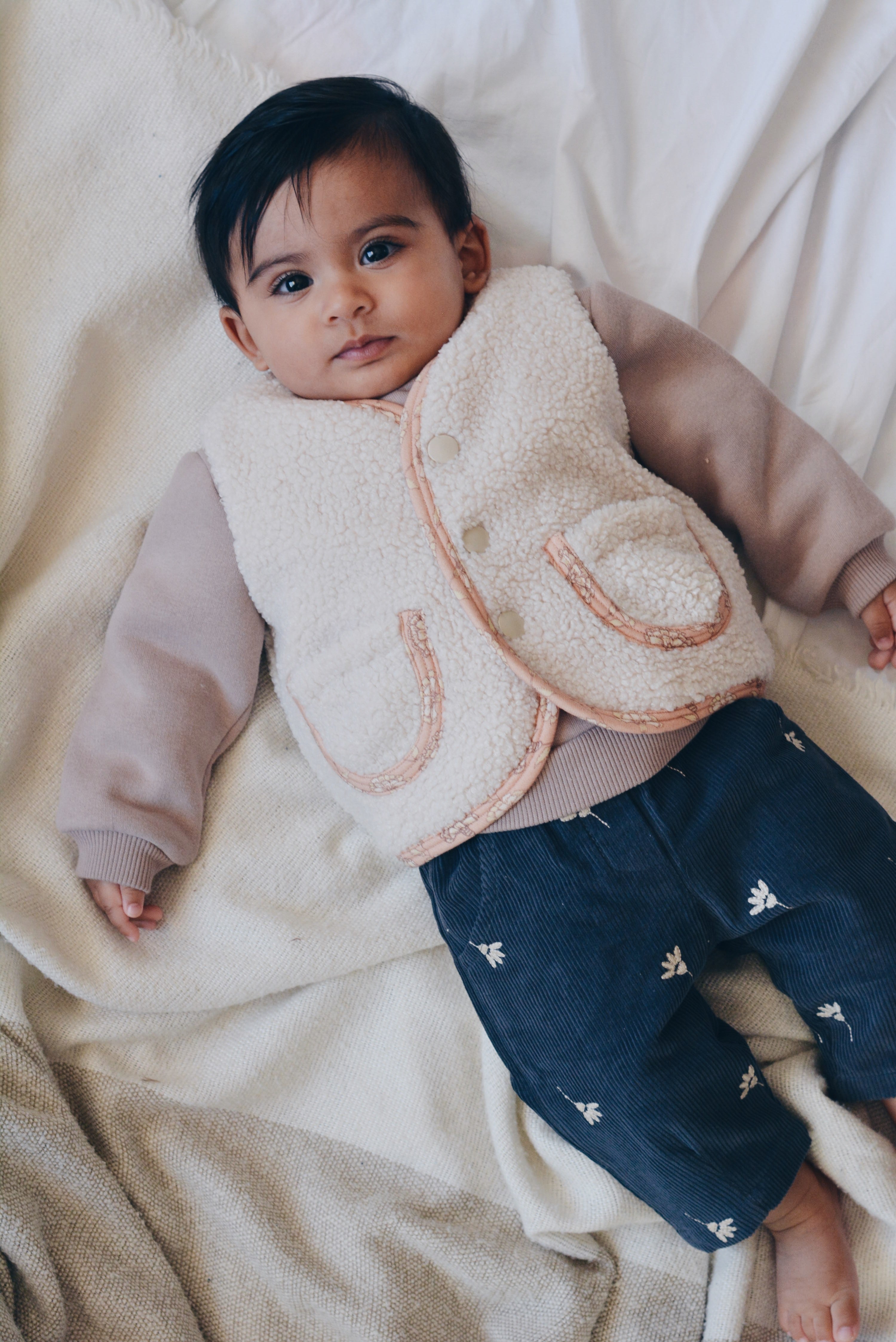 Baby Girl Wearing Rosalie Teddy Vest – Cozy Cream Sleeveless Baby Vest with Pink Floral Lining, Perfect Fall & Winter Layering, Eco-friendly