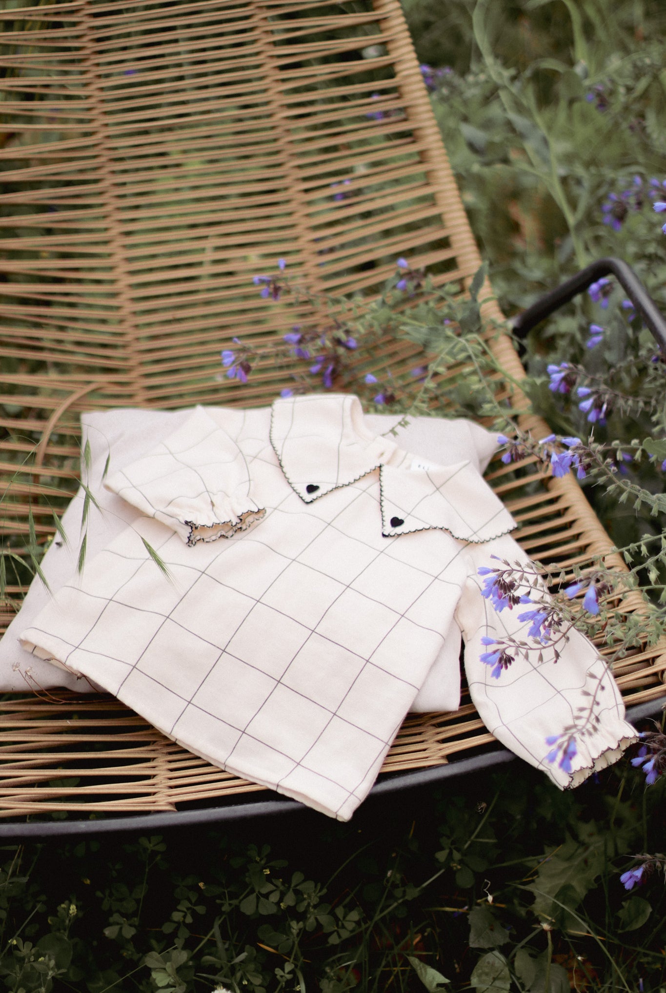 Shop the DALILA Blouse by Eli & Nev — a baby and toddler blouse in 100% OEKO-TEX certified cotton. Designed with a faded black check on beige, black trim with heart embroidery, elastic cuffed sleeves, and coconut button closure. Ethically made in Turkey, perfect for stylish and comfortable everyday wear. European baby clothing gift